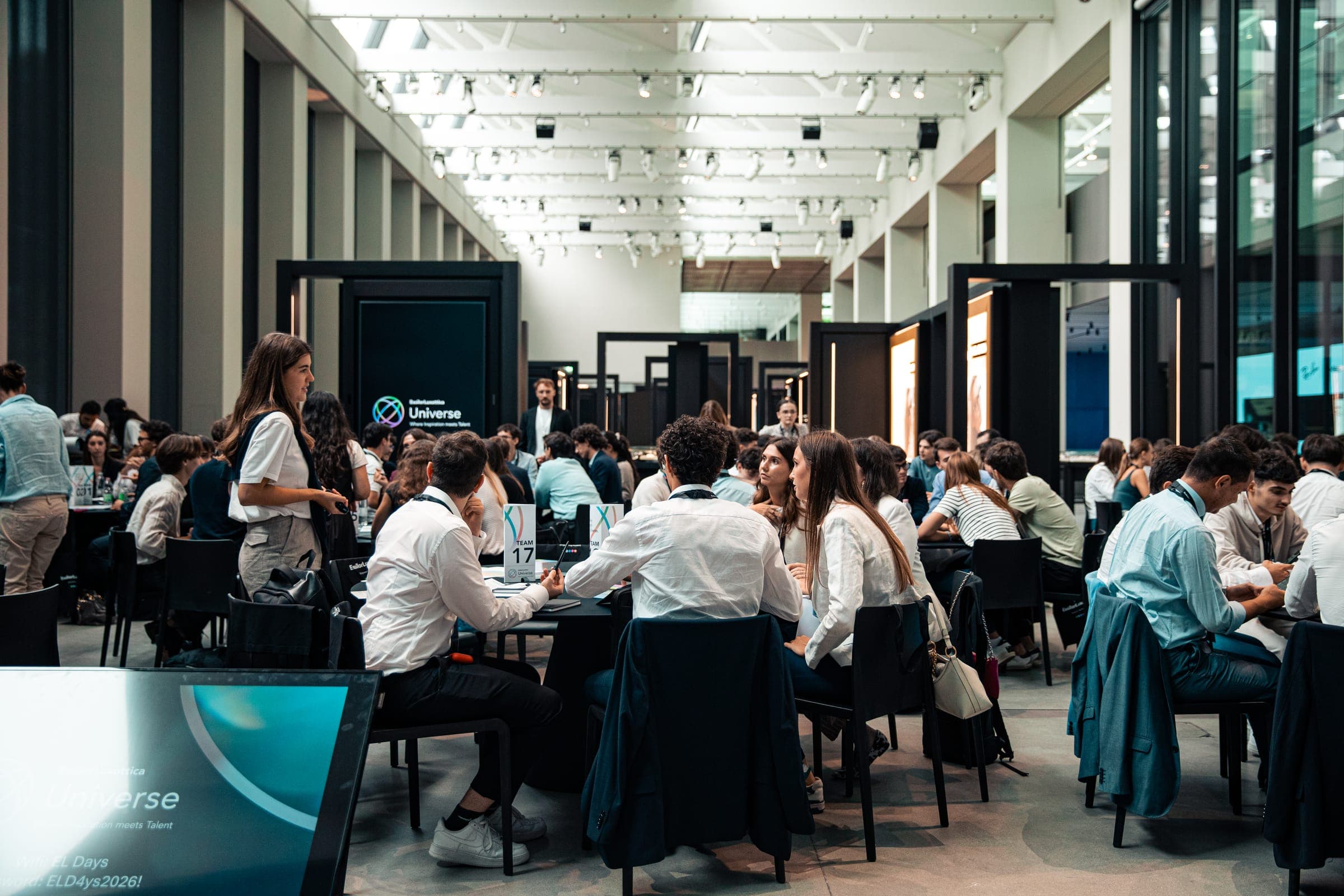 Studenti al lavoro in gruppi attorno a tavoli rotondi in un ampio spazio luminoso